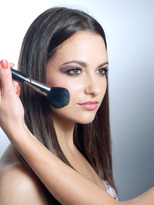 A woman has makeup applied to her face with a blush brush.