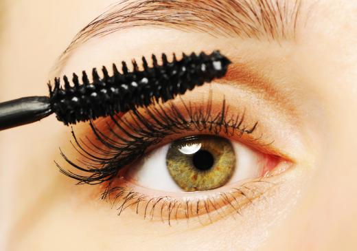 A woman applying mascara to her eyelashes with a straight brush.