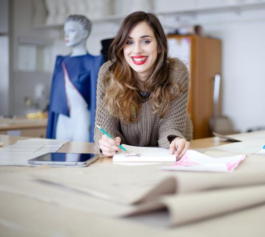 An assistant fashion designer cuts and pieces together a sewing pattern under the supervision of a senior designer.