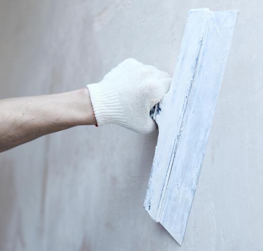 A drywall installer applies a finish coating to a wall after repairing it.