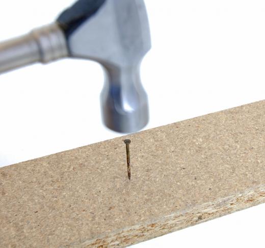 A nail being driven into a piece of chipboard.